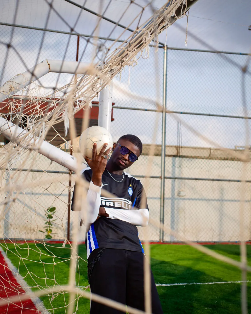 A young man poses with a football in the net of a goal.